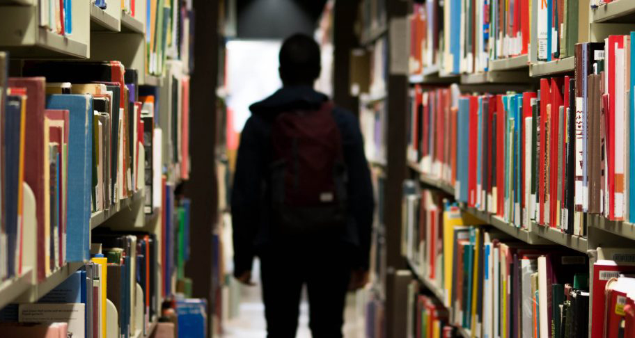 A student walking between shelves in a library.