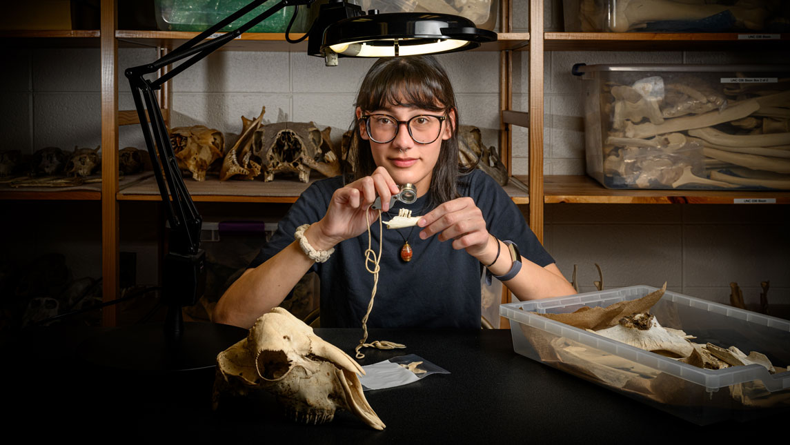 UNCG undergraduate researcher Maegan Ferguson sitting at a table examining an animal skull.