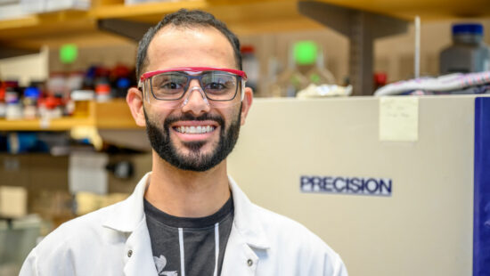 A portrait photo of David Tanas standing in front of a large, square piece of lab equipment.