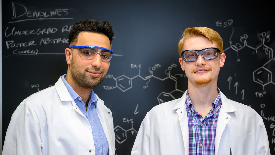 Students Abraham Ustoyev and Philip West stand in front of a blackboard.