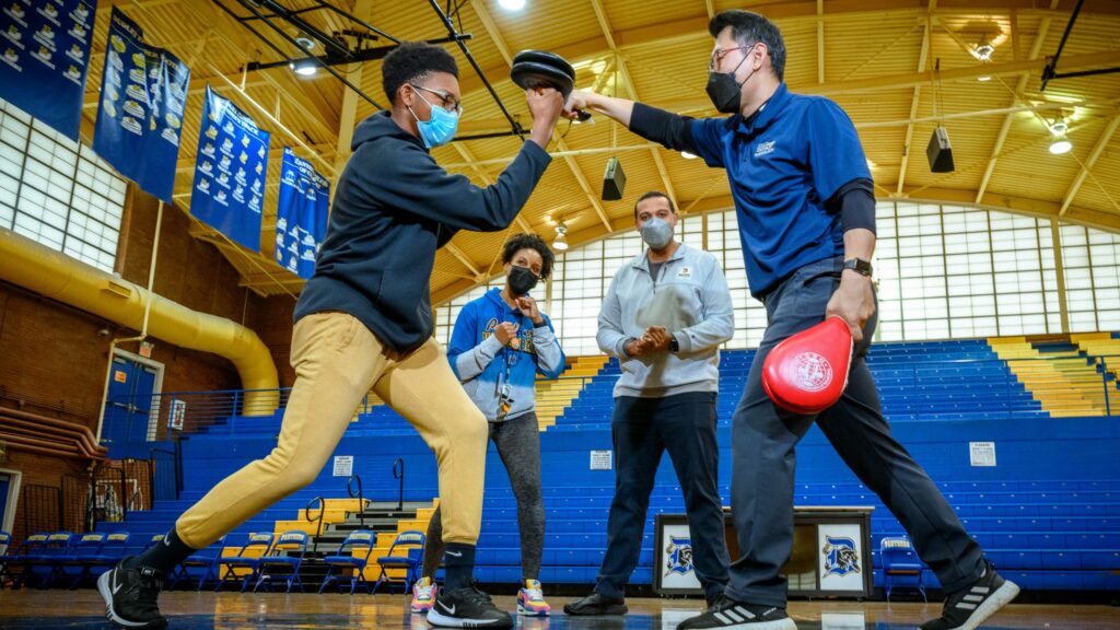 A student spars with a martial arts instructor in a gymnasium