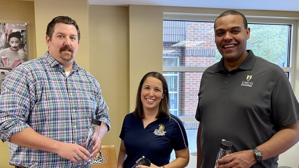 two men and a woman smile in the Military Affiliated Service building in UNCG