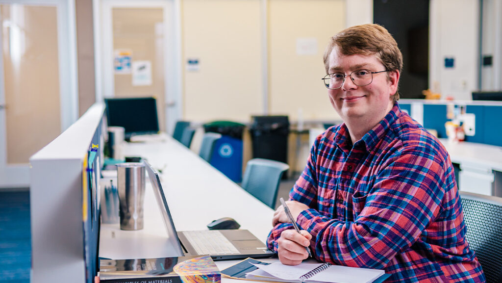 Student smiles next to his laptop