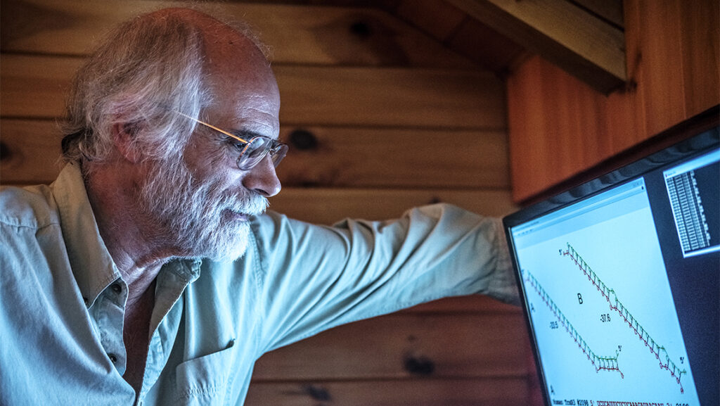 Bearded Man looks at computer screen with data.