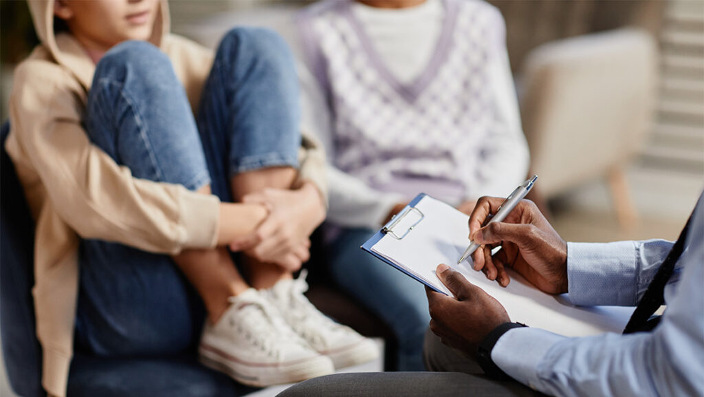 Mental health provider writing on clipboard while talking to two patients