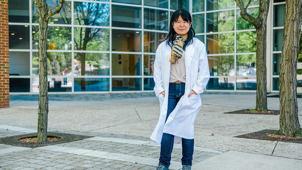 Runzi Li wearing a labcoat in front of UNCG building