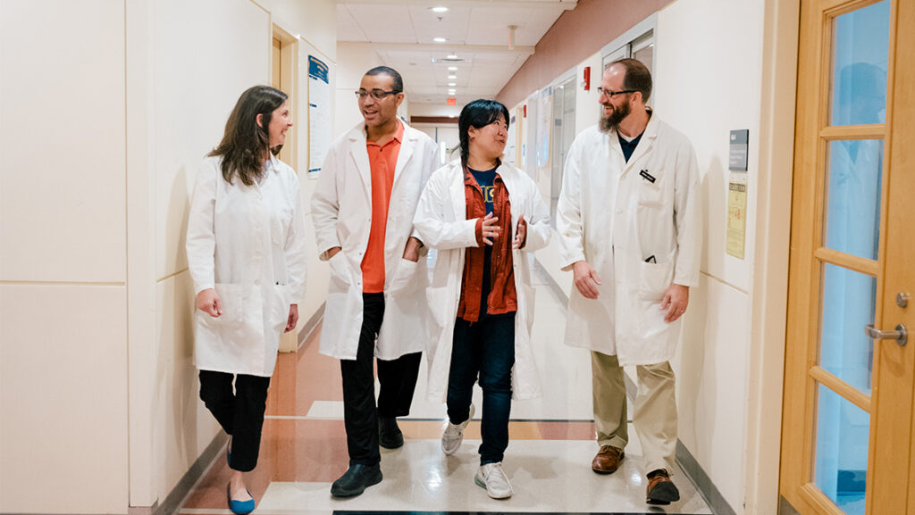Biochem students wearing lab coats walking in UNCG's Sullivan Building
