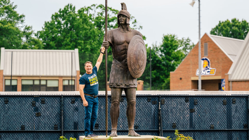 Dr. Mike Perko fist bumping a Spartan statue on UNCG's campus