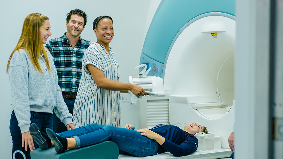 Three people standing next to a person laying down in an MRI