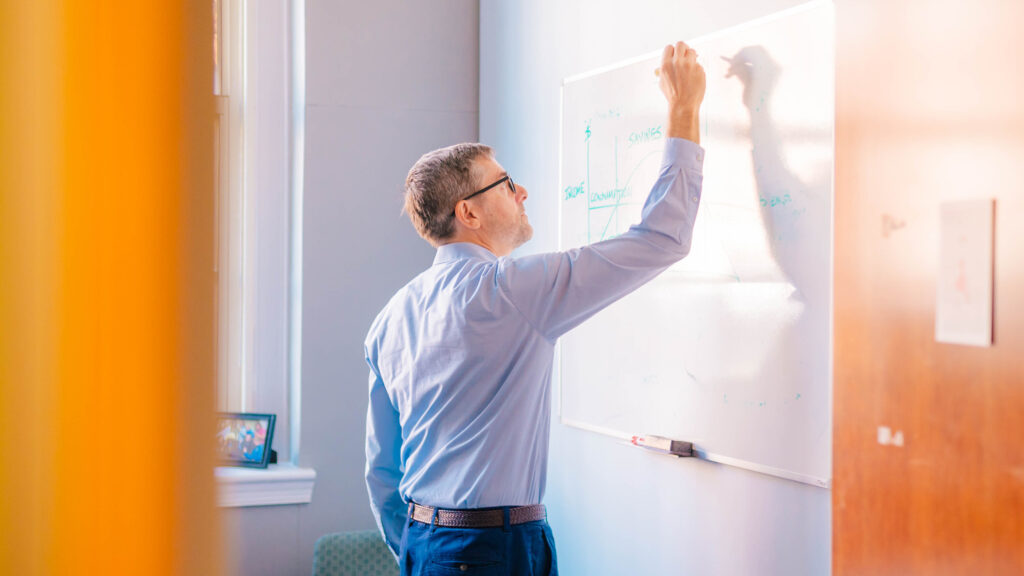 Dr. Mathieu Despard working on financial calculations on a whiteboard