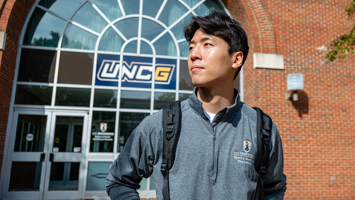 Athlete, YJ Seo, stands in front of a UNCG building.