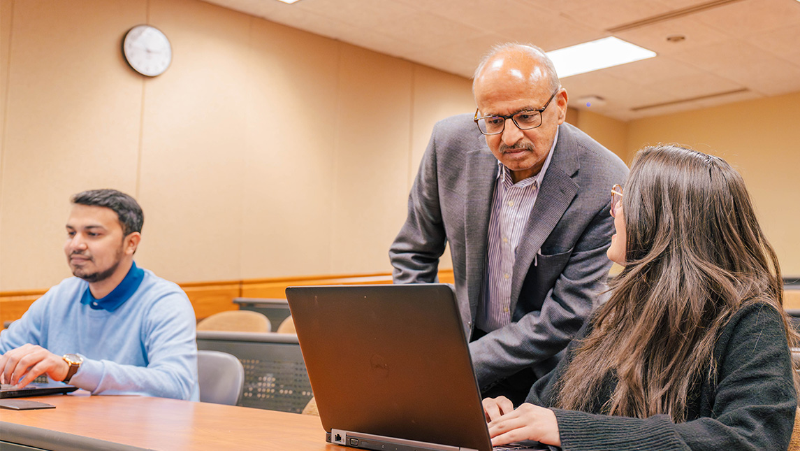 Professor looks at a computer over the shoulder of a student.