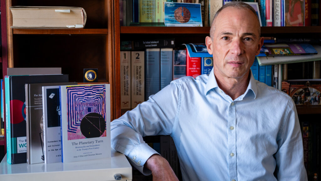 Dr. Christian Moraru posing at a bookshelf with several books