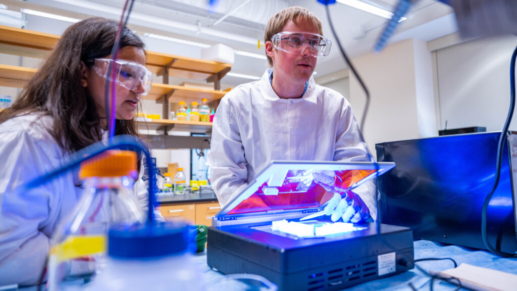 Jonathan Chekan and student using a machine in the lab