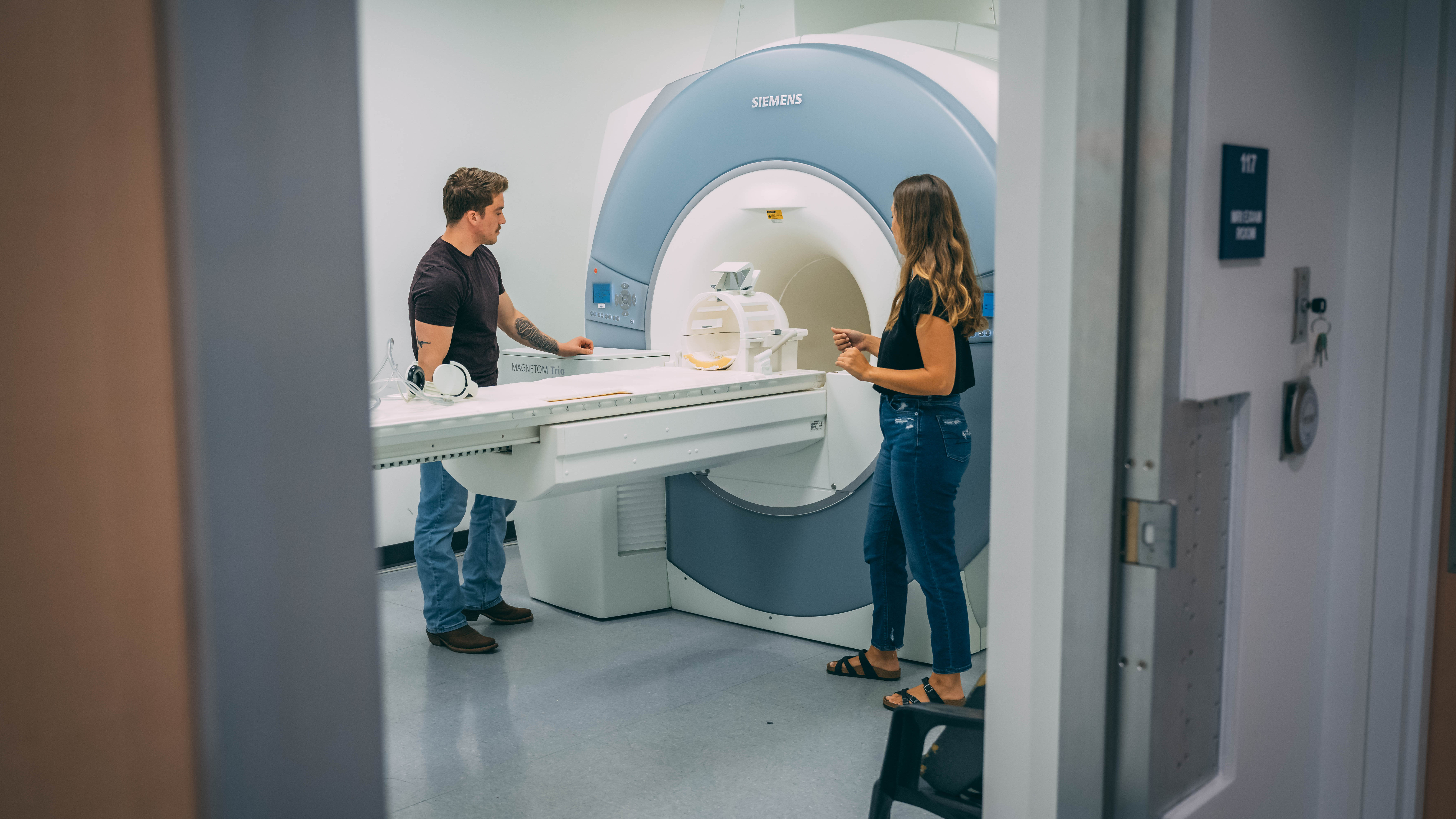 Two people stand at the entrance of an MRI machine and monitor a patient