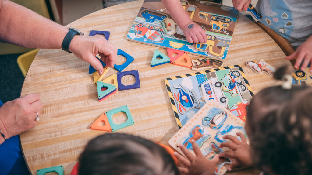 Hands of adult and several young children work on puzzles together at a table