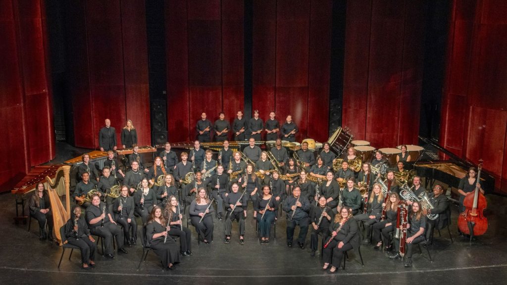 School of music's wind ensemble pose with their instruments on the stage