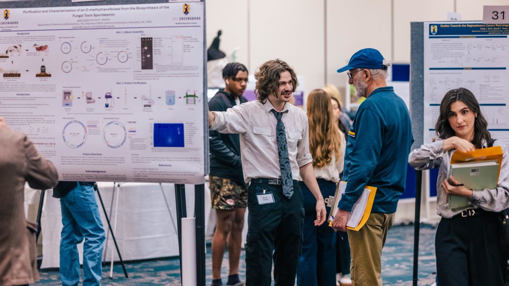 A student talks while gesturing at his poster