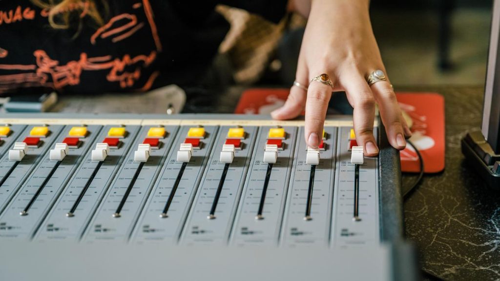 Hand adjusting sliders on an audio mixing console with colorful control buttons.