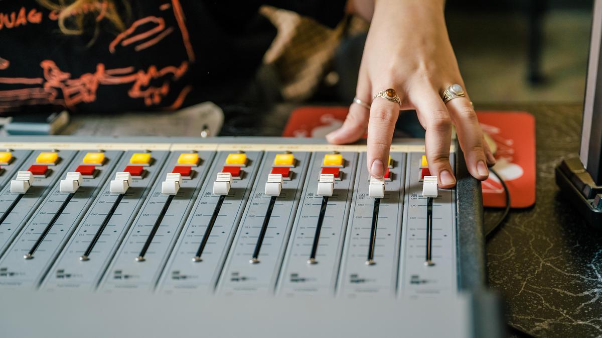 Hand adjusting sliders on an audio mixing console with colorful control buttons.