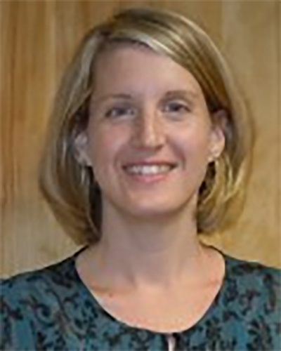 Professional portrait of Laurie Allen with short, light-colored hair, wearing a patterned top, pictured in front of a wooden background.